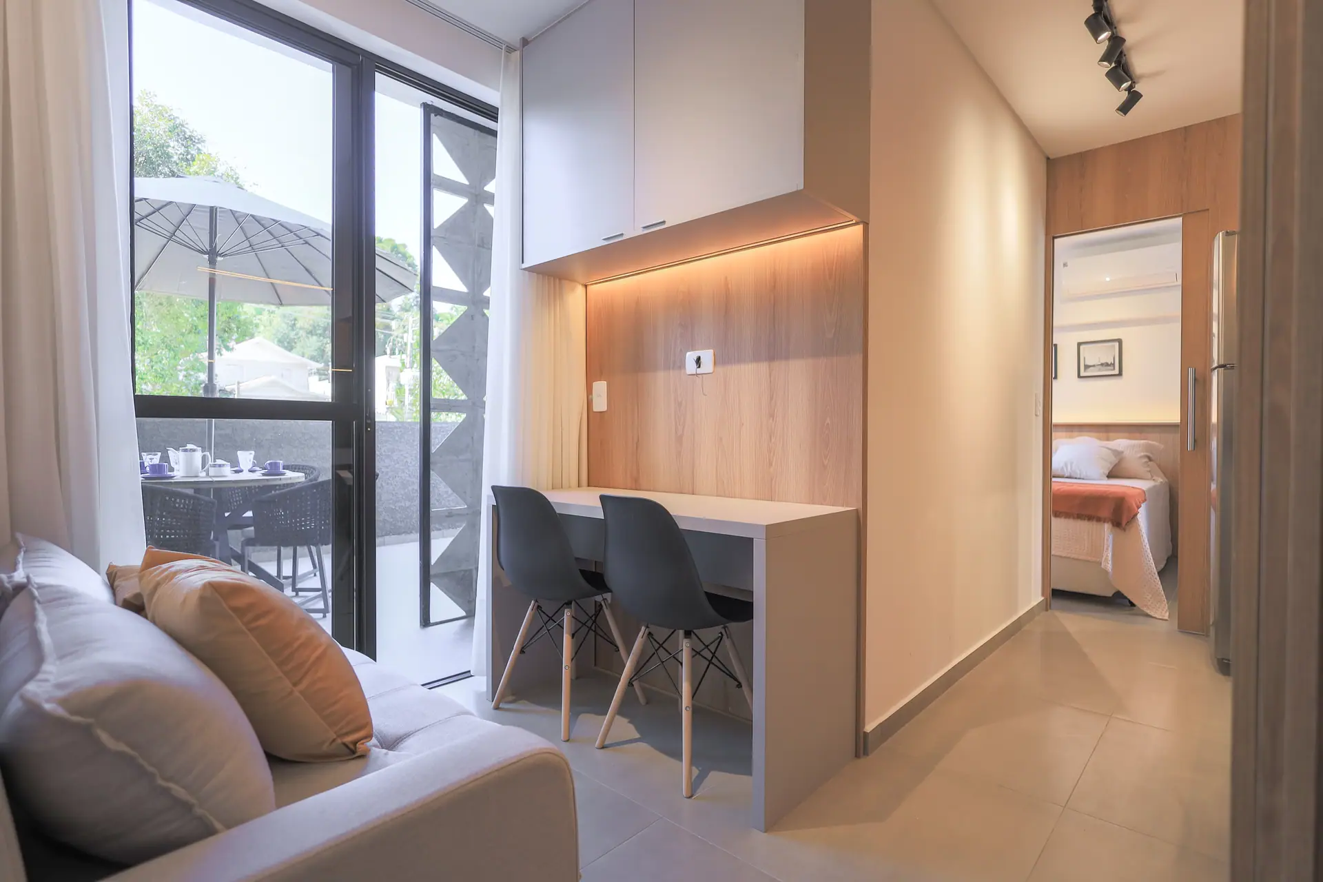 Sala com sofá e bancada, porta de vidro para o terraço e o quarto ao fundo.