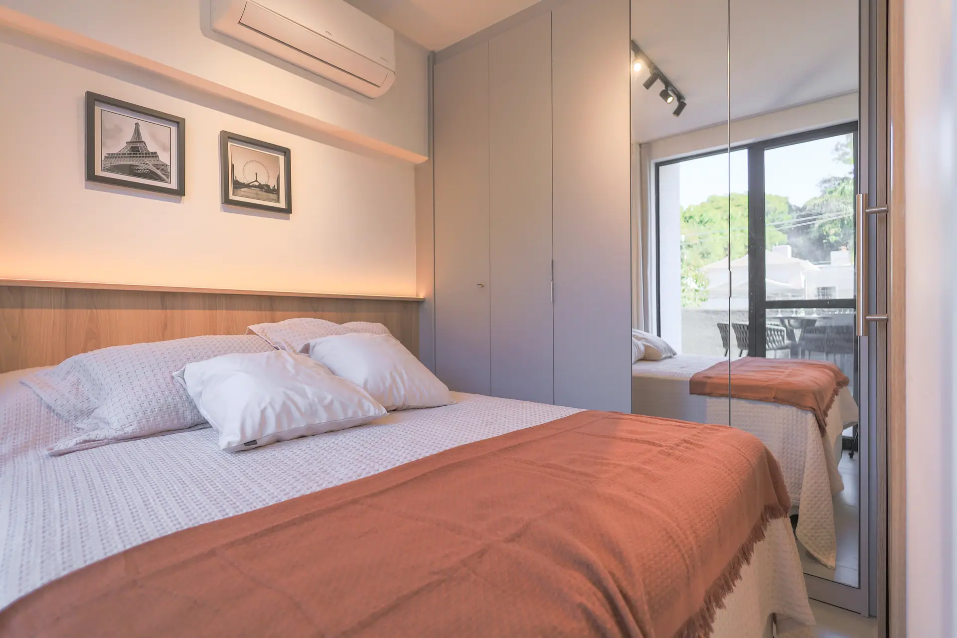 Cama com almofadas brancas, manta e armário ao lado da janela.