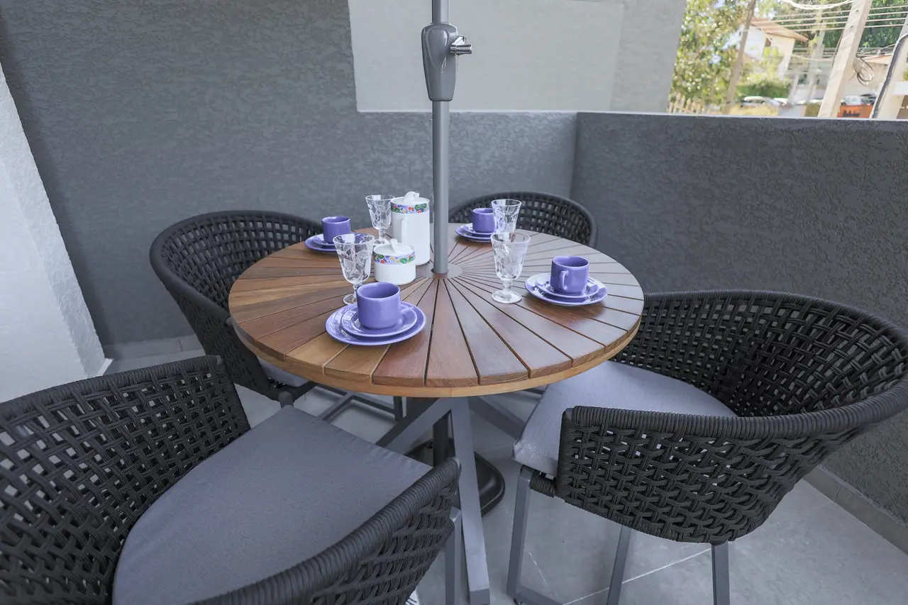 Mesa redonda de madeira posta para o café no terraço, com cadeiras trançadas.