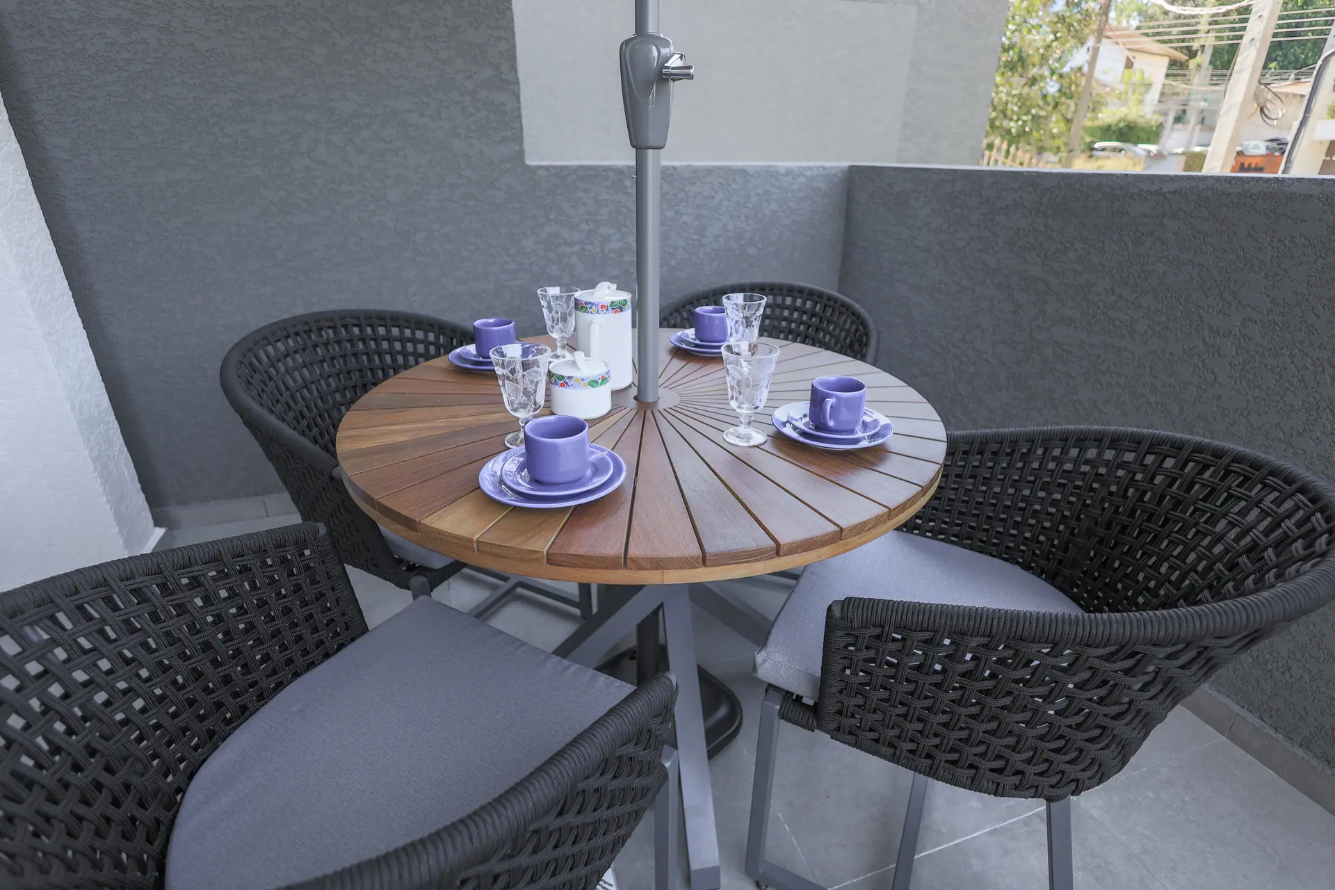 Mesa redonda de madeira posta para o café no terraço, com cadeiras trançadas.
