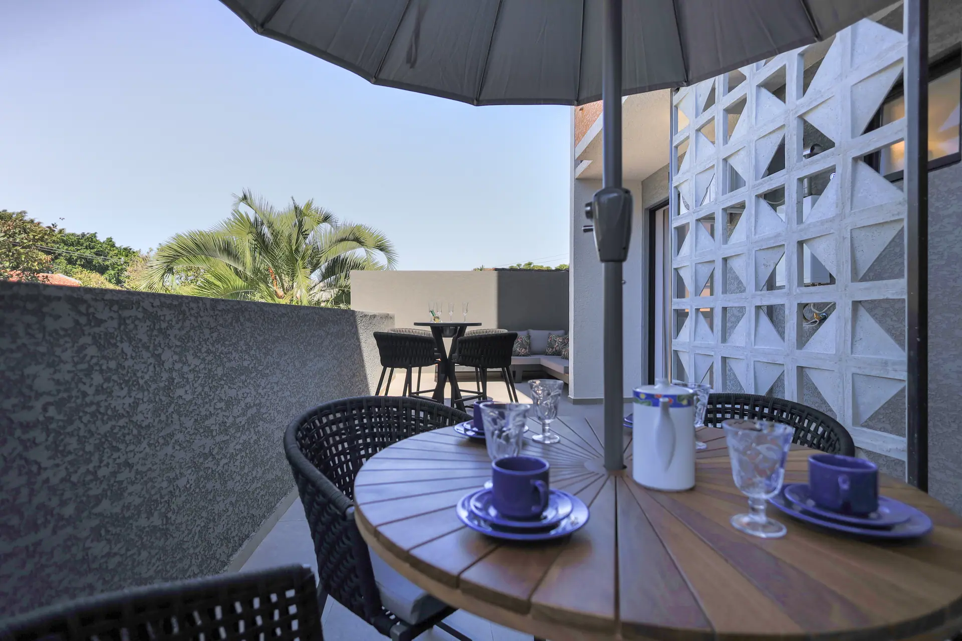 Terraço com ombrelone, mesa posta e parede de cobogó.
