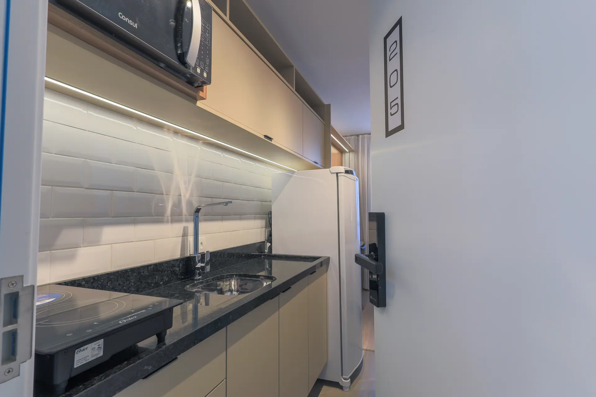 Cozinha linear com bancada escura, cooktop e fita de luz sob o armário.