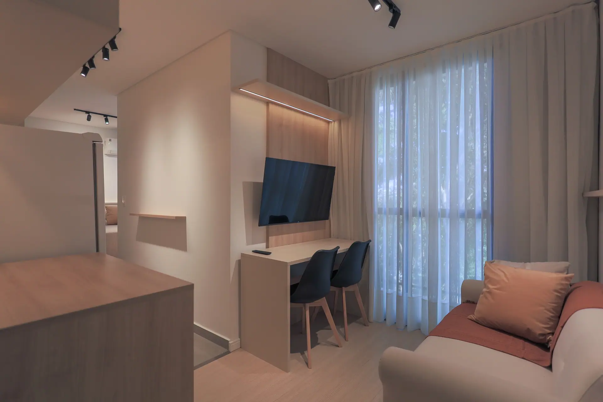Sala vista da cozinha: bancada, TV, sofá e janela com cortina.