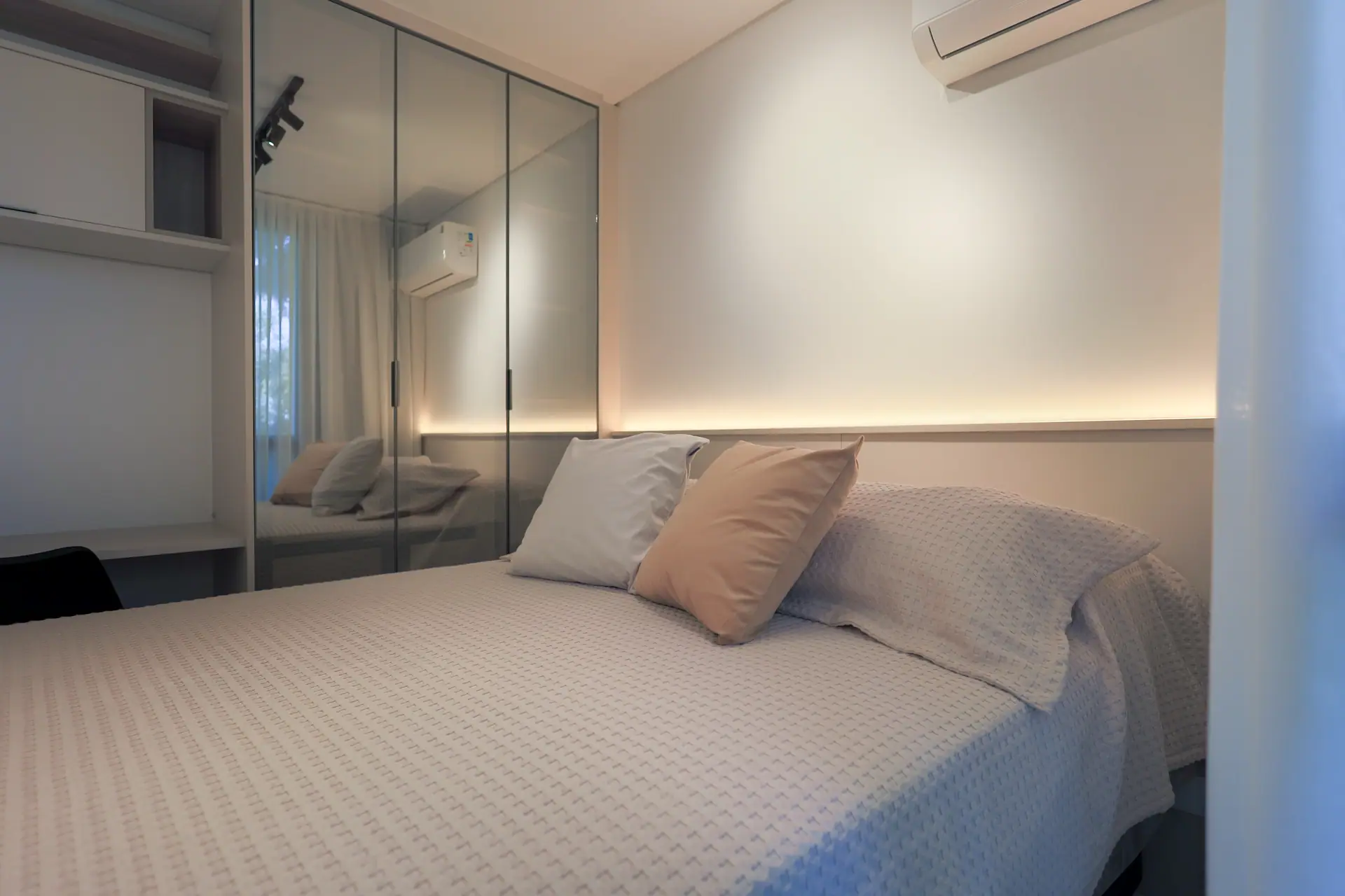 Cama com almofadas ao lado do armário espelhado.